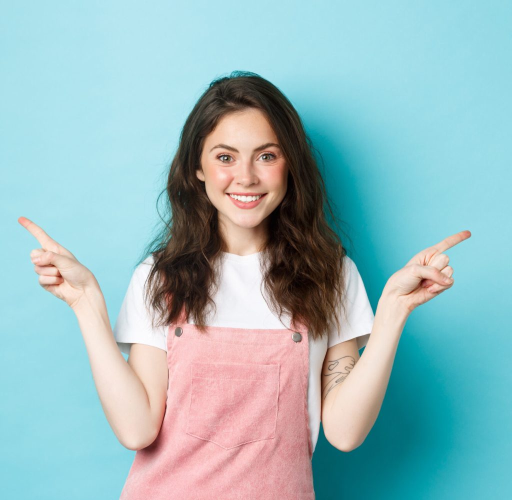 Image of glamour beautiful girl with bright make up, pointing fingers sideways and smiling, showing two variants of promo offers, give choices, blue background Image of glamour beautiful girl with bright make up, pointing fingers sideways and smiling, showing two variants of promo offers, give choices, blue background.